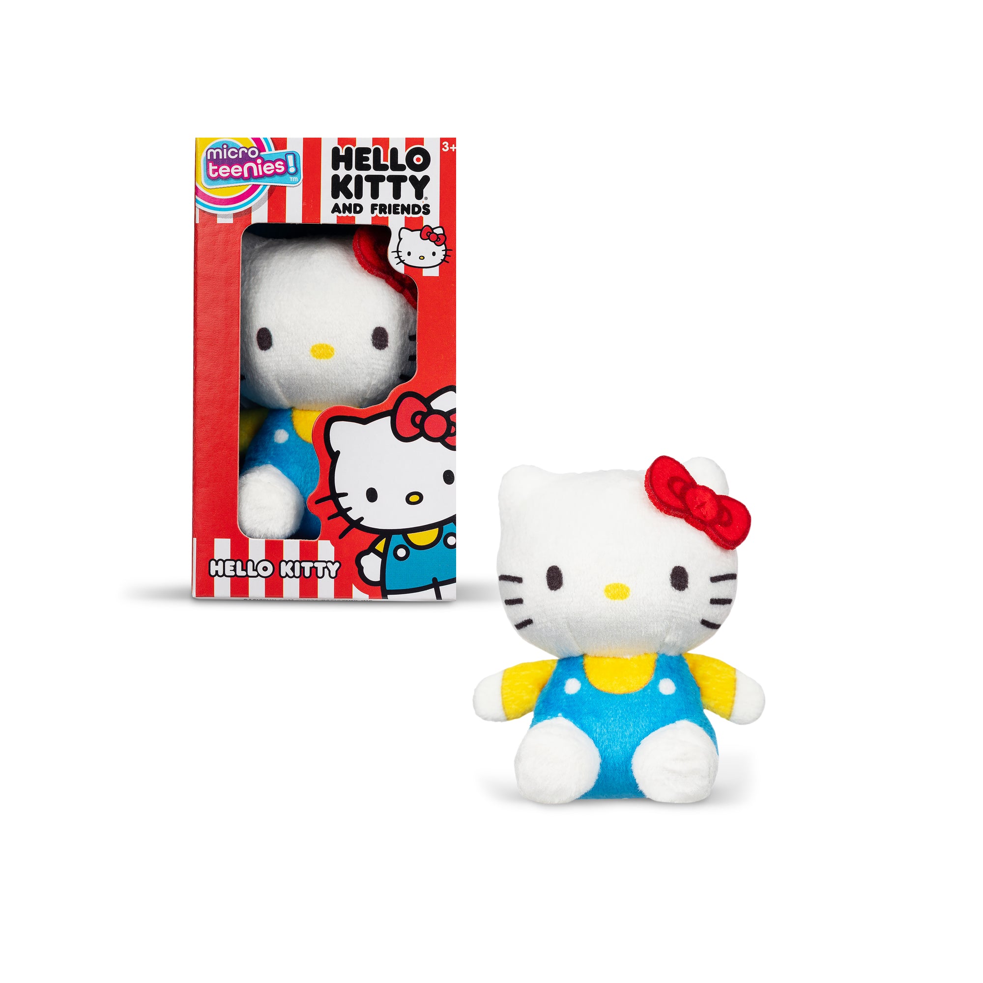 A Hello Kitty plush toy sits outside its box. The toy is white with a red bow on its head, and it wears a blue dress with yellow sleeves. The box features the Hello Kitty logo and an illustration of the character, with red and black striped sides.